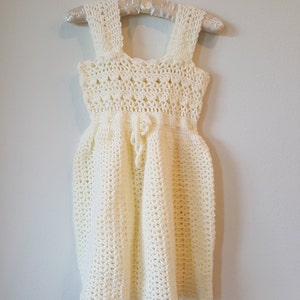 May include: A white crocheted dress with a square neckline and a tie at the waist.