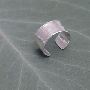 Puede incluir: Un anillo de plata martillado con un acabado texturizado. El anillo está abierto y tiene una forma ligeramente curvada.