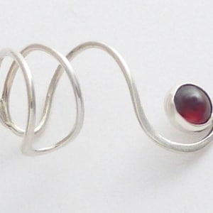 May include: A silver-colored metal ring featuring a spiral design that wraps around the finger. The band extends into a curved arm that terminates in a single, round, deep red gemstone set in a smooth, polished silver-colored metal bezel.