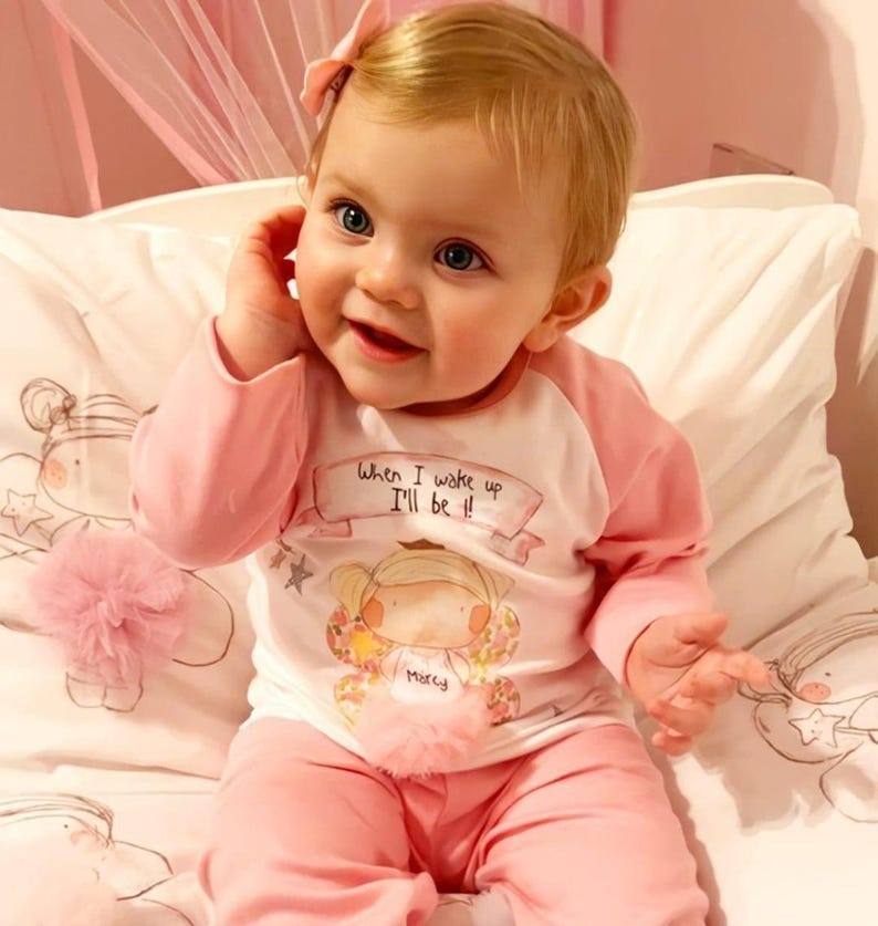 Pu&ograve; includere: Una bambina che indossa un pigiama rosa e bianco con un'immagine di una ragazza con il testo "Quando mi sveglio, sar&ograve;!" e il nome "Molly".