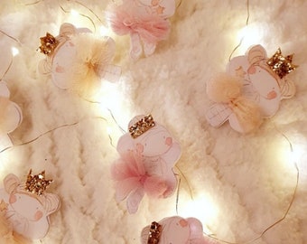 Può includere: Una ghirlanda di luci fatate con ornamenti di ballerina rosa e dorati. Ogni ornamento presenta una ballerina con una corona e una gonna di tulle.