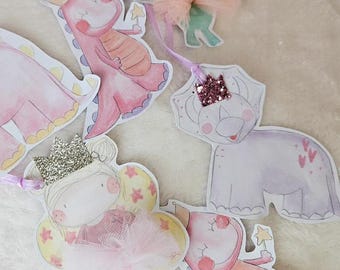 May include: A set of five pink and purple watercolor-style paper cutouts featuring a fairy, a dinosaur, a dragon, and two triceratops. The cutouts are strung together with a purple ribbon and have glitter accents.