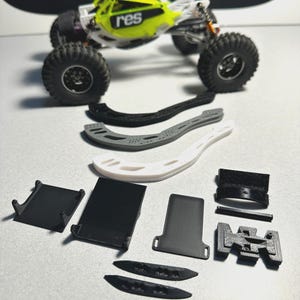 以下が含まれることがあります： 大きな黒いタイヤと「res」の文字が入った、ライムグリーンと黒のリモコンカー。シャーシコンポーネントや取り付けブラケットなど、さまざまな黒、白、グレーの3Dプリントパーツが車の下に配置されています。