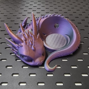 Könnte beinhalten: Ein lilafarbener und schillernder Drachen-Pflanztopf mit einer runden Öffnung oben. Der Topf ist aus einem glatten, glänzenden Material gefertigt und hat ein detailliertes Drachen-Design.
