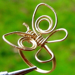May include: A gold wire butterfly ring with a delicate design. The ring is made of thin wire that is twisted and shaped to create the butterfly's wings and body.