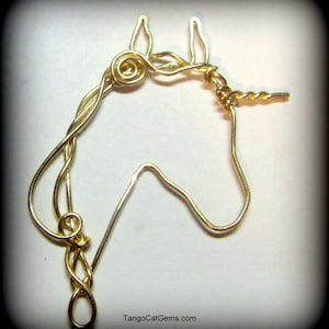 Peut inclure: Sculpture en fil de fer doré représentant une tête de licorne avec une corne torsadée. La sculpture est sur un fond blanc. TangoCatGems.com est imprimé sous la sculpture.