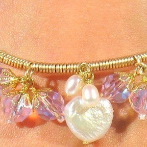 May include: A gold charm bracelet with pink and white iridescent beads and heart-shaped charms.
