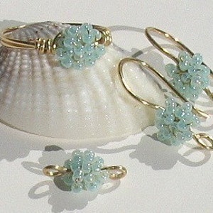 May include: A set of three jewelry pieces featuring light blue beads clustered together in a ball shape. The pieces include a ring, a pair of earrings, and a charm. The jewelry is made with gold-toned wire.