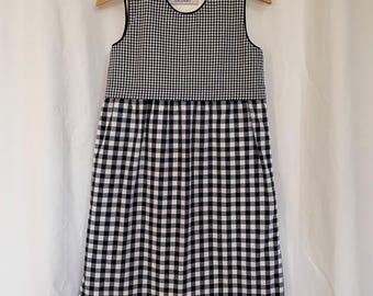 Könnte beinhalten: Ein ärmelloses Kleid in Schwarz-Weißem Gingham mit abgerundetem Saum. Das Kleid hat ein kleines weißes Etikett mit dem Text "CALENDKIDS" auf der Vorderseite.