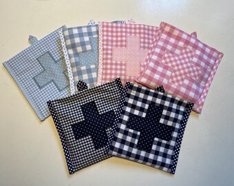 Könnte beinhalten: Fünf Stoffquadrate mit einem weißen Pluszeichen in der Mitte. Die Quadrate sind in verschiedenen Farben und Mustern: hellblaues Gingham, pinkfarbenes Gingham, schwarz-weißes Gingham und zwei schwarz-weiße Punkte.
