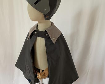 Könnte beinhalten: Ein graues und schwarzes Ritterkostüm für Kinder, bestehend aus einem Umhang und einem Helm mit Visier.