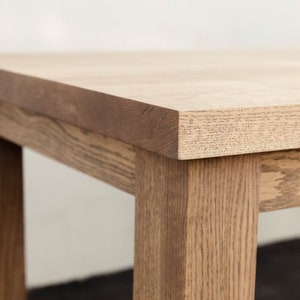 May include: Close-up of a wooden table top with a light brown finish. The table has a simple, rectangular design with visible wood grain.