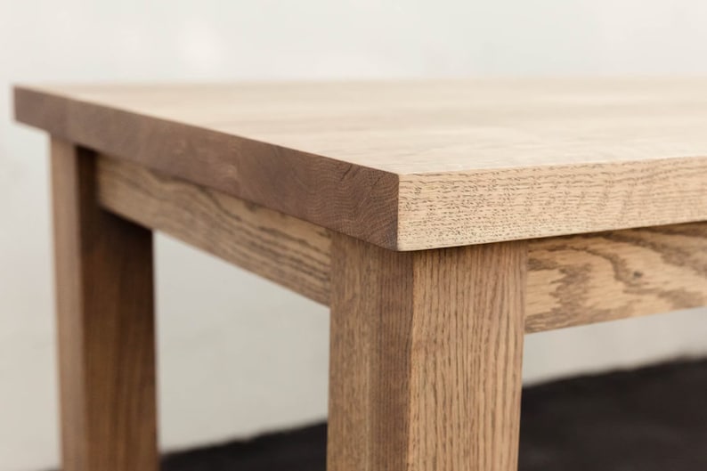 May include: Close-up of a wooden table top with a light brown finish. The table has a simple, rectangular design with visible wood grain.