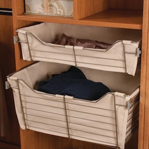 May include: Two beige fabric-lined wire baskets with metal frames are pulled out from a wooden closet shelf. The baskets are stacked on top of each other. The top basket is empty and the bottom basket contains a folded blue sweater.
