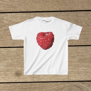 May include: White t-shirt with a red raspberry printed on the front. The raspberry is in the shape of a heart.