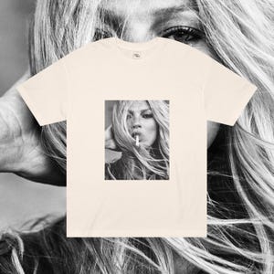 May include: A cream-colored t-shirt with a black and white photo of a woman with long hair smoking a cigarette.