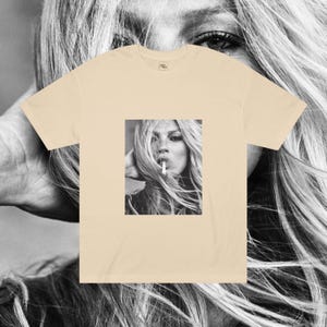 May include: A beige t-shirt with a black and white photo of a woman with long hair smoking a cigarette.