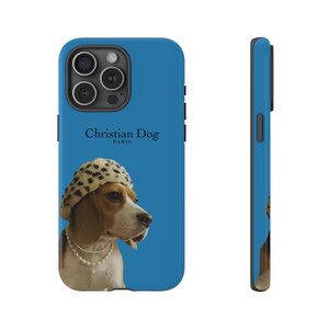 Peut inclure: Une coque de téléphone bleue avec un beagle portant un chapeau à pois noirs et blancs. Le texte "Christian Dog Paris" est imprimé sur la coque.