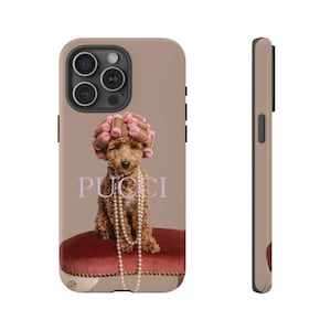 Könnte beinhalten: Ein brauner und weißer Hund mit rosa Lockenwicklern auf dem Kopf sitzt auf einem roten Samtstuhl. Der Hund trägt eine Perlenkette und der Hintergrund ist hellbraun. Der Text "PUCCI" ist in Lila auf dem Hintergrund gedruckt.
