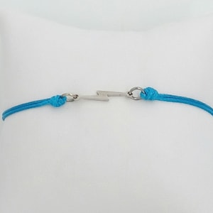May include: A turquoise blue string bracelet with a silver lightning bolt charm.