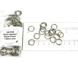 May include: Two bags of 100 silver-finished jump rings, each measuring 12mm in diameter and made with 1.5mm wire. The jump rings are displayed next to a ruler for size reference.