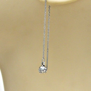 May include: Silver chain earrings with a small, textured ball at the end. The earrings are hanging from a model's ear.