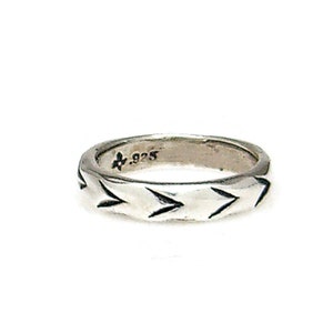 May include: A silver band ring with a textured design of arrows pointing in one direction. The ring is marked with the number .925.
