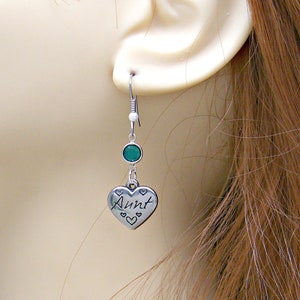 May include: Silver heart-shaped earrings with the word "Aunt" inscribed on the front. The earrings feature a green gemstone and a silver hook.