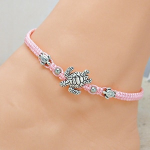 May include: Pink braided anklet with silver turtle charms. The anklet has small silver beads between the charms.