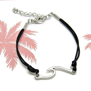 May include: A black cord bracelet with a silver wave charm. The bracelet has a lobster clasp closure.