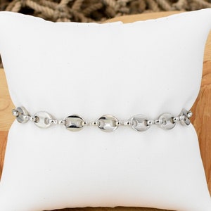 May include: A silver chain bracelet with oval links. The bracelet is displayed on a white pillow.