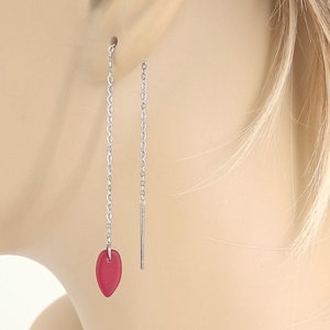 May include: A pair of silver dangle earrings with a red heart-shaped charm at the end of each chain.