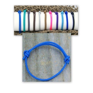 May include: A close-up of a blue paracord bracelet with a knot on the side. The bracelet is on a wooden surface.