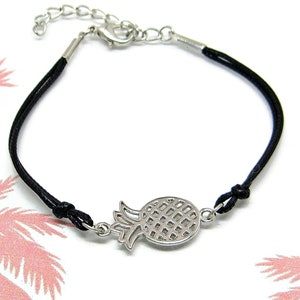 May include: A black cord bracelet with a silver pineapple charm. The charm is detailed with a textured pineapple design.