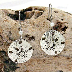 May include: Silver dangle earrings featuring a sand dollar design with a small pearl accent.