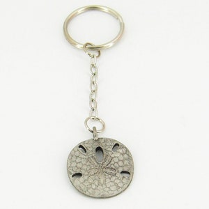 May include: A silver key chain with a sand dollar charm. The sand dollar has a detailed design and five holes.