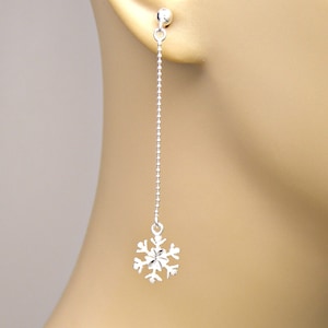 May include: A single silver earring with a snowflake pendant. The earring hangs from a delicate chain of small beads, attached to a ball stud. The snowflake design is detailed and intricate, with multiple points.