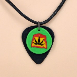 May include: A black guitar pick necklace with a green circle pendant featuring a black marijuana leaf design on a red and yellow background.