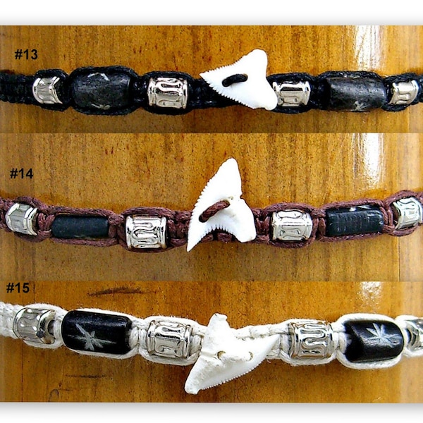 May include: Three bracelets with black, brown, and white cords. Each bracelet has a shark tooth charm, black beads, and silver beads. The bracelets are numbered #13, #14, and #15.