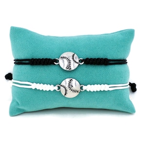 May include: Two friendship bracelets with baseball charms. One bracelet is black and the other is white.