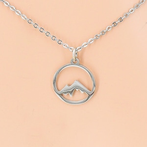 May include: A silver necklace with a circular pendant featuring a cut-out mountain design.