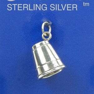 Könnte beinhalten: Sterling-Silber-Anhänger einer kleinen, silbernen Metalltasse mit abgerundetem Boden und leicht ausgestelltem oberen Rand. Der Anhänger befindet sich auf einem blauen Hintergrund mit dem Text "Silverado Sterling Silver" und "Janice Marie Peek".