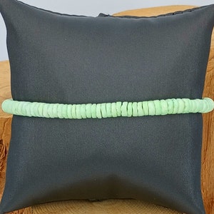 May include: A light green beaded bracelet made of small, round beads. The bracelet is displayed on a black pillow.