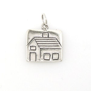May include: A silver charm in the shape of a house with a chimney and windows. The charm is square and has a textured surface.