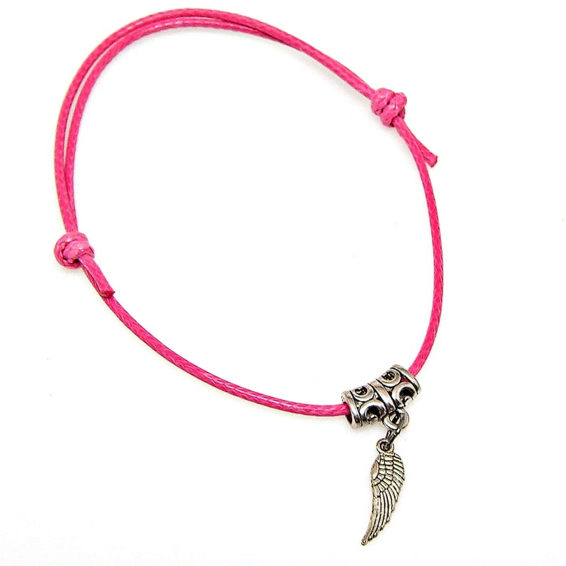 May include: A pink cord bracelet with a silver charm featuring an angel wing. The charm is attached to the cord with a silver bead.