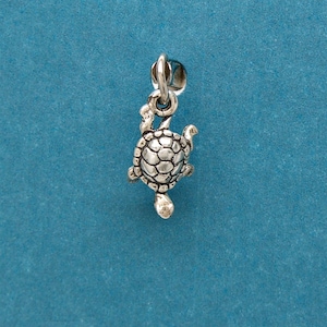 May include: A silver charm in the shape of a turtle. The turtle is facing to the right and has a detailed shell.