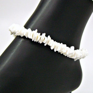 May include: White shell anklet made of small, irregular pieces of white shell. The anklet is shown on a black mannequin leg.