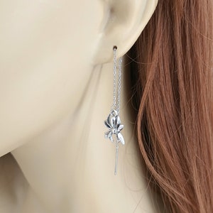 May include: Silver dangle earrings with a delicate flower charm hanging from a chain. The earrings are long and flowy, perfect for adding a touch of elegance to any outfit.