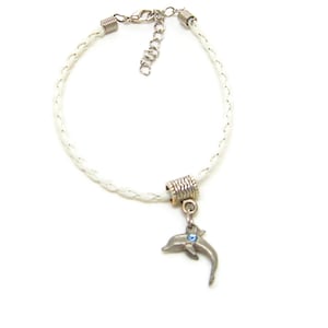 May include: White braided leather bracelet with a silver dolphin charm. The dolphin has a blue rhinestone eye.