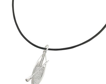 May include: Silver-tone pendant necklace featuring a detailed canoe and paddle design. The pendant hangs from a black cord. The canoe has a textured surface, and the paddle is positioned across the canoe. The necklace is set against a white background.